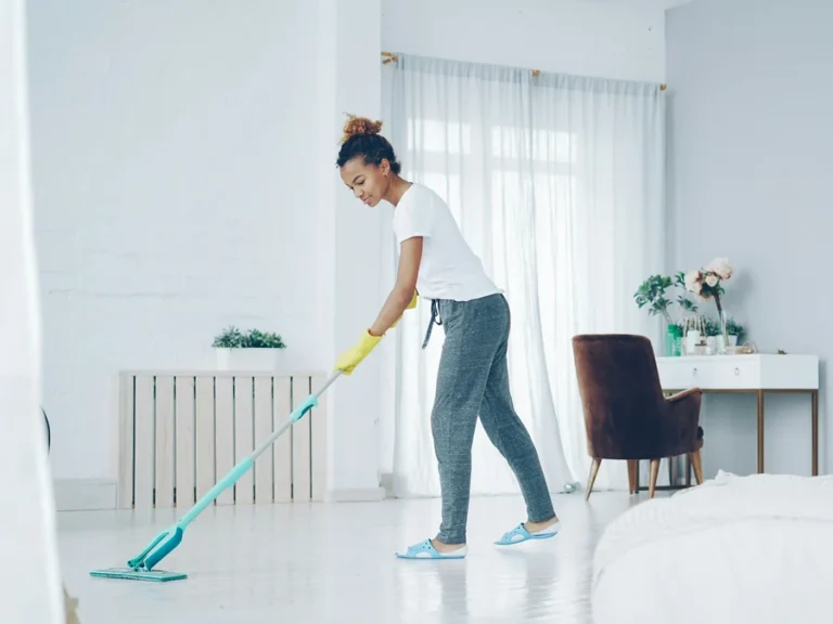 House cleaning: young woman in yellow gloves mopping the pale floor of a bright living room