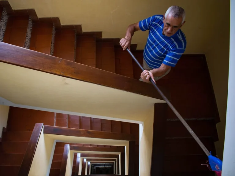 Nettoyage d'immeubles : homme lavant au balai les paliers d'une cage d'escalier commune